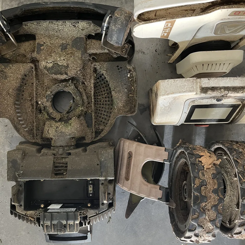 Robot rasaerba smontato in officina, scocca lame e ruote appoggiate a terra